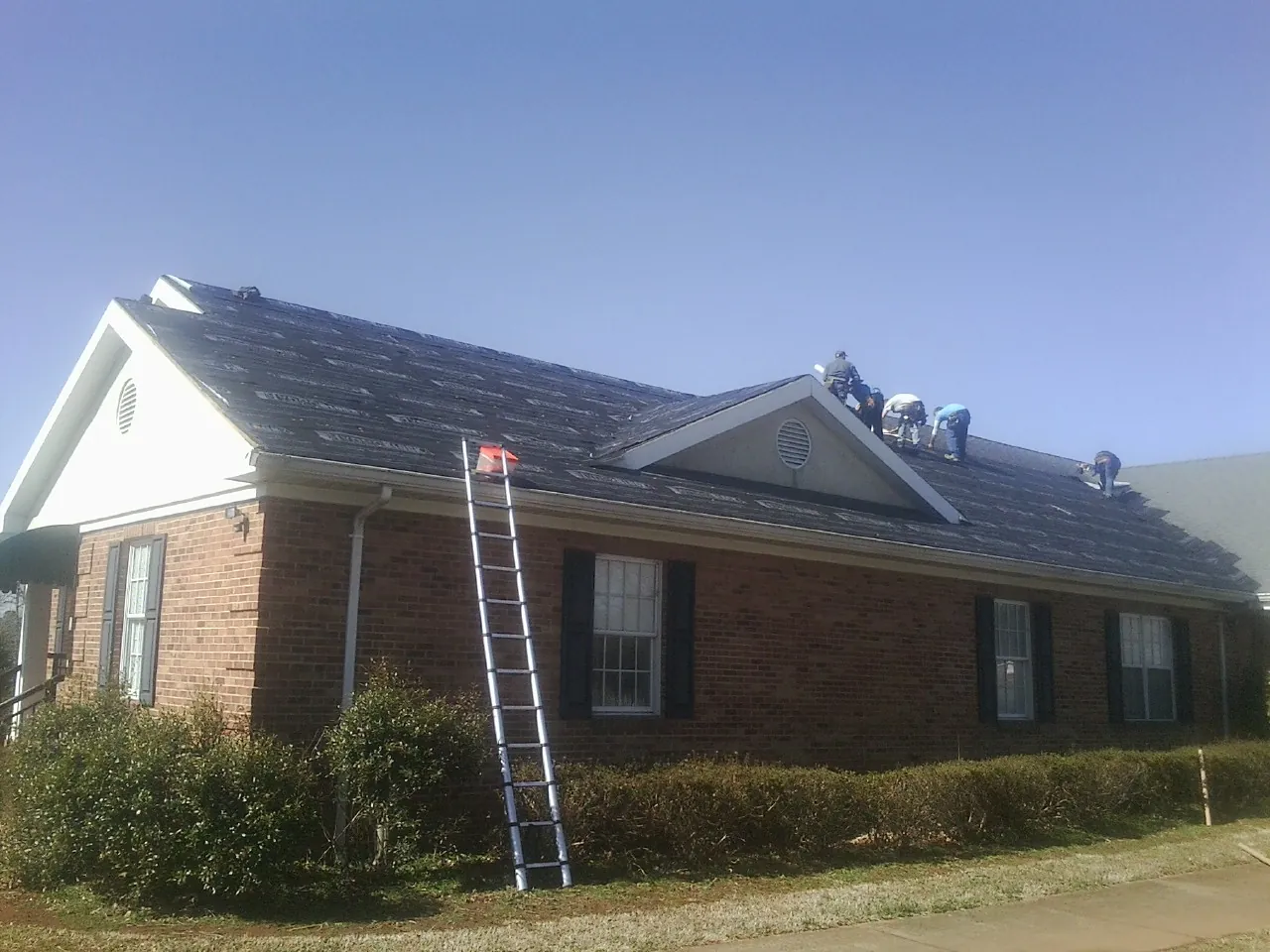 Crew tearing shingles off a brick ranch roof with a ladder set — Emergency Roof Repair work by our crew in Danbury