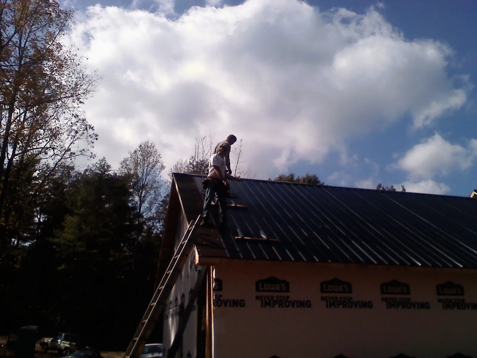Roofer fastening dark metal panels high against a cloudy sky, from a Roof Inspection job in Danbury